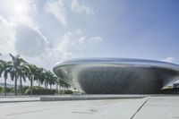 a large circular building sitting next to palm trees in a courtyard with blue sky and sun