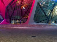 a street next to a building with an upside down skylight above it that is lit up pink and blue