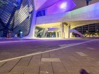 the modern building has a tall curved structure over it with neon lights on it at night