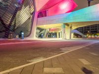 the modern building has a tall curved structure over it with neon lights on it at night