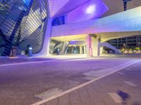 the modern building has a tall curved structure over it with neon lights on it at night