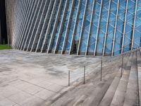 steps leading up to a very large modern building with many diagonal glass walls behind it