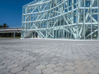 a large modern glass building is on the side of a brick road with a person standing next to it