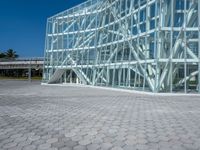 a large modern glass building is on the side of a brick road with a person standing next to it