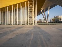 a yellow modern building sitting inside of it's open air structure with tall metal poles