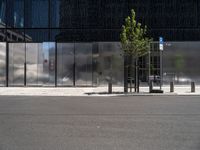 a parked car next to a tall grey building with some sort of wall and two trees in front of the building