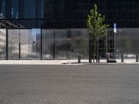 a parked car next to a tall grey building with some sort of wall and two trees in front of the building