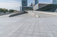 a skate boarder performing tricks on the cement in front of a building with many high rise buildings and trees