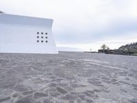 a concrete structure with seven spots on it's outside wall near water and a building