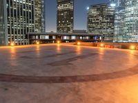 the circular cement surface has lights shine on it and looks out over the city from behind it