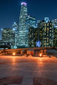 a city skyline with buildings lit up at night from an empty platform overlooking the ground