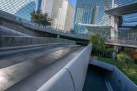 large modern buildings are shown behind an empty walkway and a water way near a green park