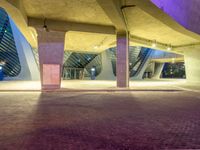 the buildings are very lit up against the blue sky above them and under it are several purple concrete pillars