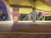 the buildings are very lit up against the blue sky above them and under it are several purple concrete pillars