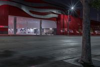 a bus drives past a large red building with white panels at night time on the street