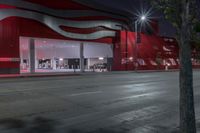 a bus drives past a large red building with white panels at night time on the street