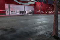 a bus drives past a large red building with white panels at night time on the street