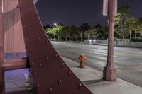 a brown fire hydrant standing next to a bridge at night with street and trees