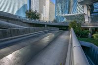 a paved road in front of a tall buildings and trees, which give off an illusion of the view through the walkways of the sidewalks