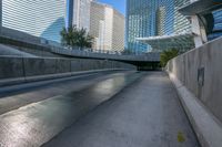 a paved road in front of a tall buildings and trees, which give off an illusion of the view through the walkways of the sidewalks