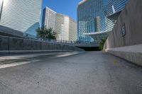 a paved road in front of a tall buildings and trees, which give off an illusion of the view through the walkways of the sidewalks