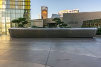 large gray bench in front of modern building with trees next to it in plaza area