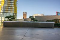 large gray bench in front of modern building with trees next to it in plaza area