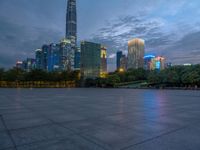 a paved patio surrounded by tall buildings at dusk time with a bench to sit on