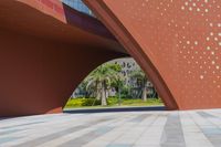 a brown building has a geometric design on it in an empty area with grass and palm trees