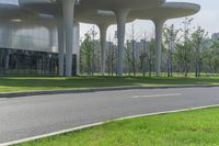 a couple of motorcycles riding down a paved road near a large building near some trees