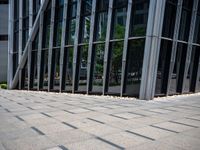 someone walking down a stone walkway in front of an office building with large windows and flooring