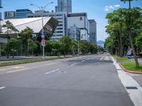 the empty road near many tall buildings is lined with trees and street signs in front of it