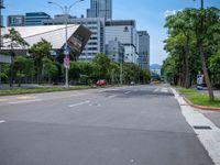 the empty road near many tall buildings is lined with trees and street signs in front of it