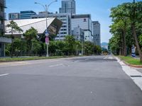 the empty road near many tall buildings is lined with trees and street signs in front of it