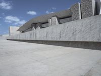 a gray cement structure sitting under a blue sky with white clouds in the background on a concrete surface