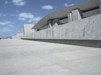 a gray cement structure sitting under a blue sky with white clouds in the background on a concrete surface