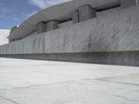 a gray cement structure sitting under a blue sky with white clouds in the background on a concrete surface