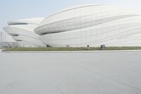 a person on a bicycle in front of an enormous building with lots of windows and curved shapes