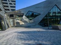 a brick courtyard near tall buildings has two geometric windows, and a bench on the side