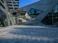 a brick courtyard near tall buildings has two geometric windows, and a bench on the side