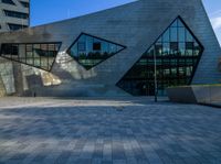 a brick courtyard near tall buildings has two geometric windows, and a bench on the side