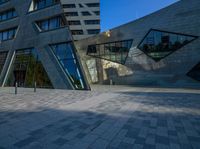 a brick courtyard near tall buildings has two geometric windows, and a bench on the side