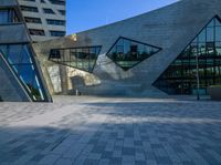 a brick courtyard near tall buildings has two geometric windows, and a bench on the side