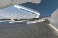 a night shot of a curved walkway at an art museum with white walls and steps that lead to a circular roof