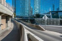 a curved, concrete road on an overpassed highway with skyscrapers in the background