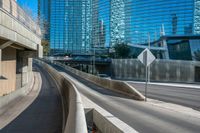 a curved, concrete road on an overpassed highway with skyscrapers in the background