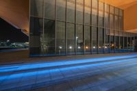 a person standing outside of a building with blue light streaming on the sidewalk at night