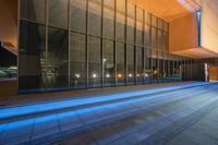 a person standing outside of a building with blue light streaming on the sidewalk at night