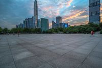 a city skyline is shown from the ground at sunset, and a person walks on the pavement