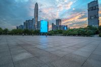 a city skyline is shown from the ground at sunset, and a person walks on the pavement